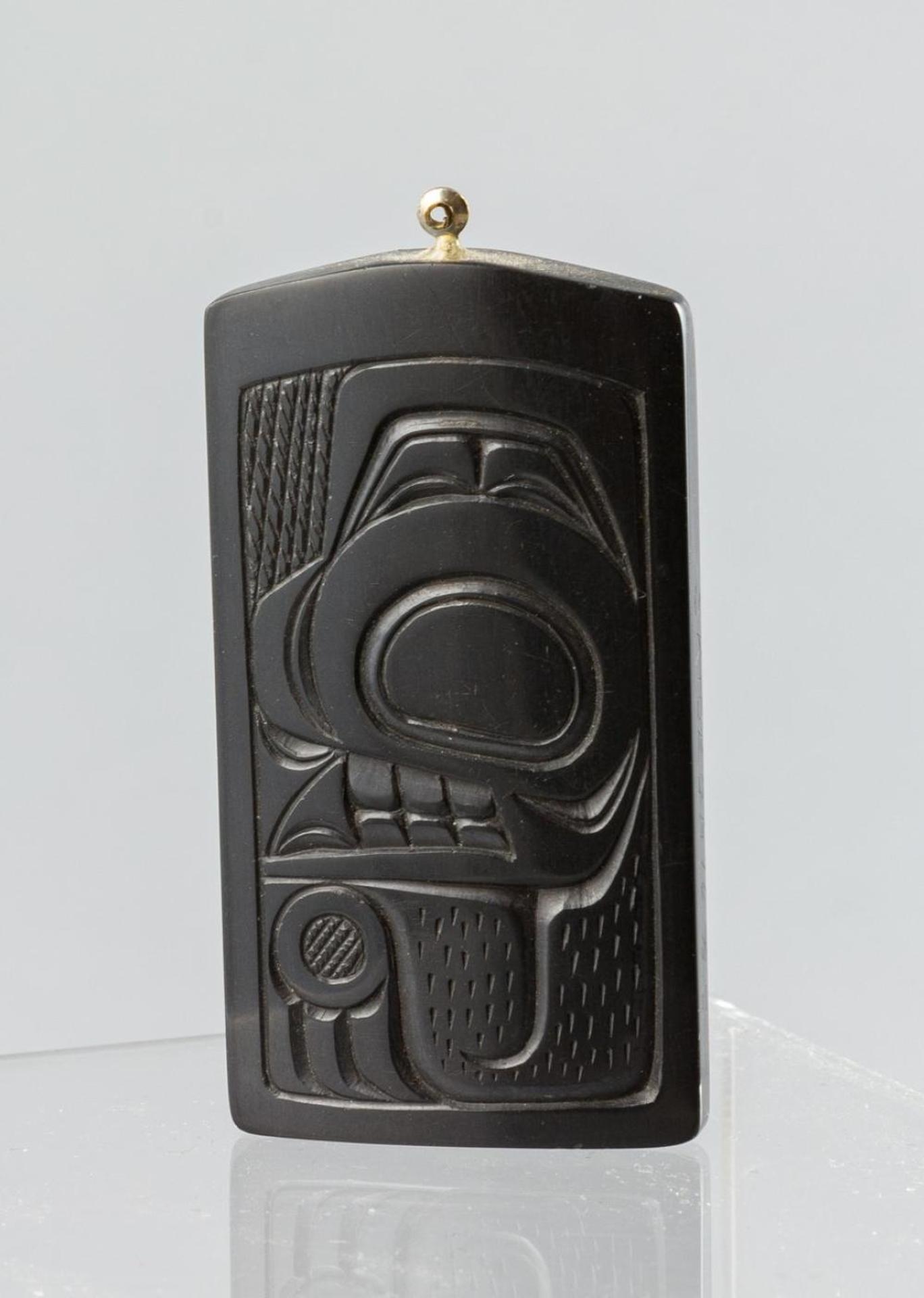 Denny Dixon (1944) - a rectangular carved argillite pendant decorated with Raven design to one side and Bear the other