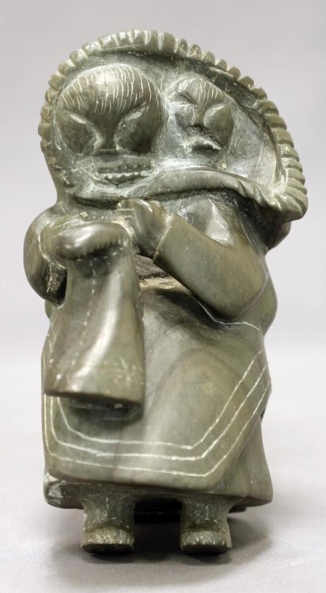 Johnassie Arragutainaq (1935) - light grey-green stone carving of a Woman With Baby in Amaut Making a Mukluk