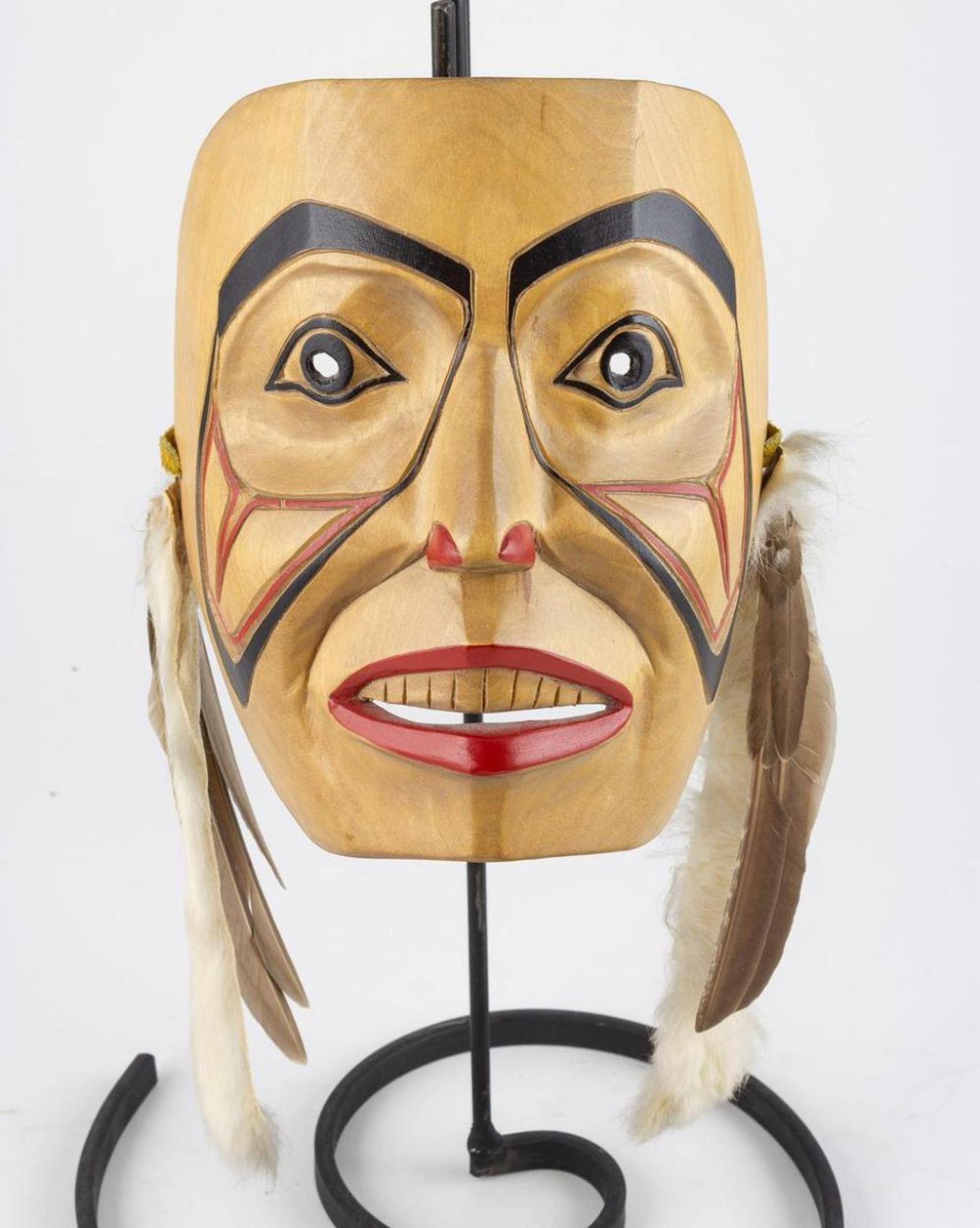 Delia O'Brien - a carved and polychromed mask decorated with feathers and fur strips