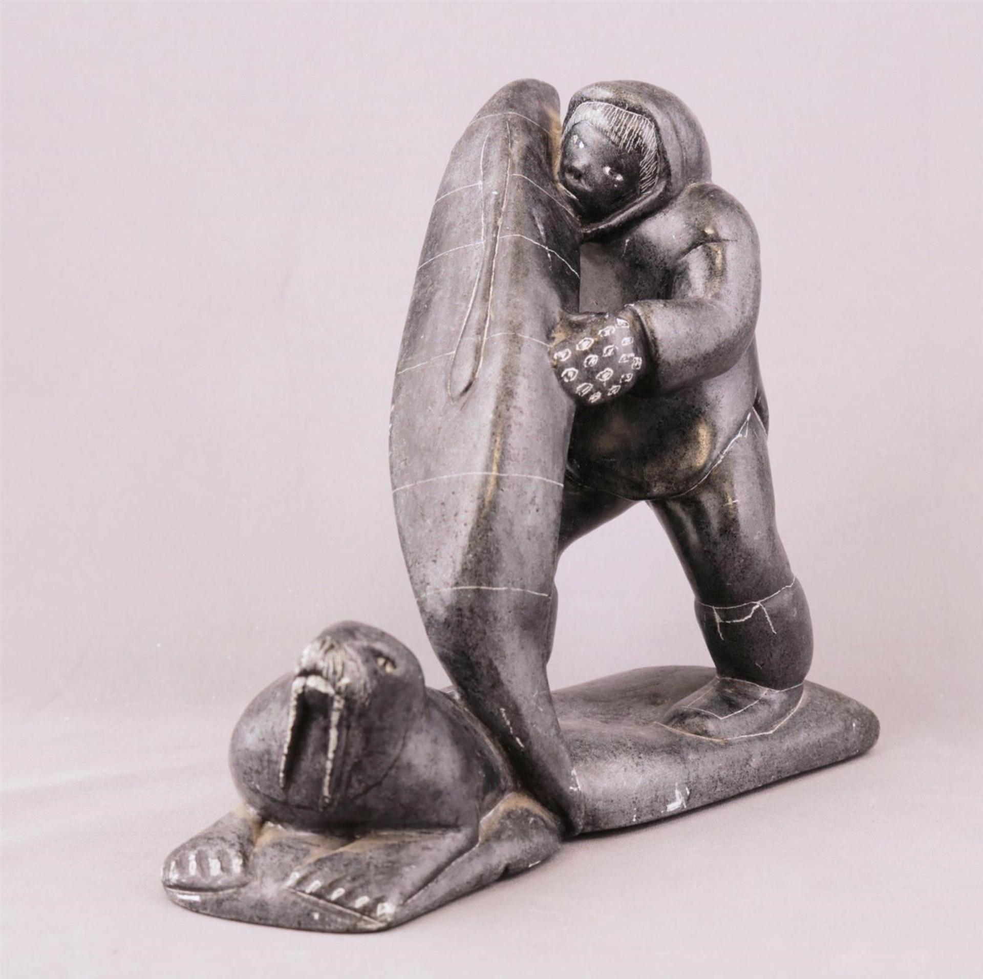 Levi Qumaluk (1919-1997) - a dark grey stone carving of a Man with a Kayak and a Walrus